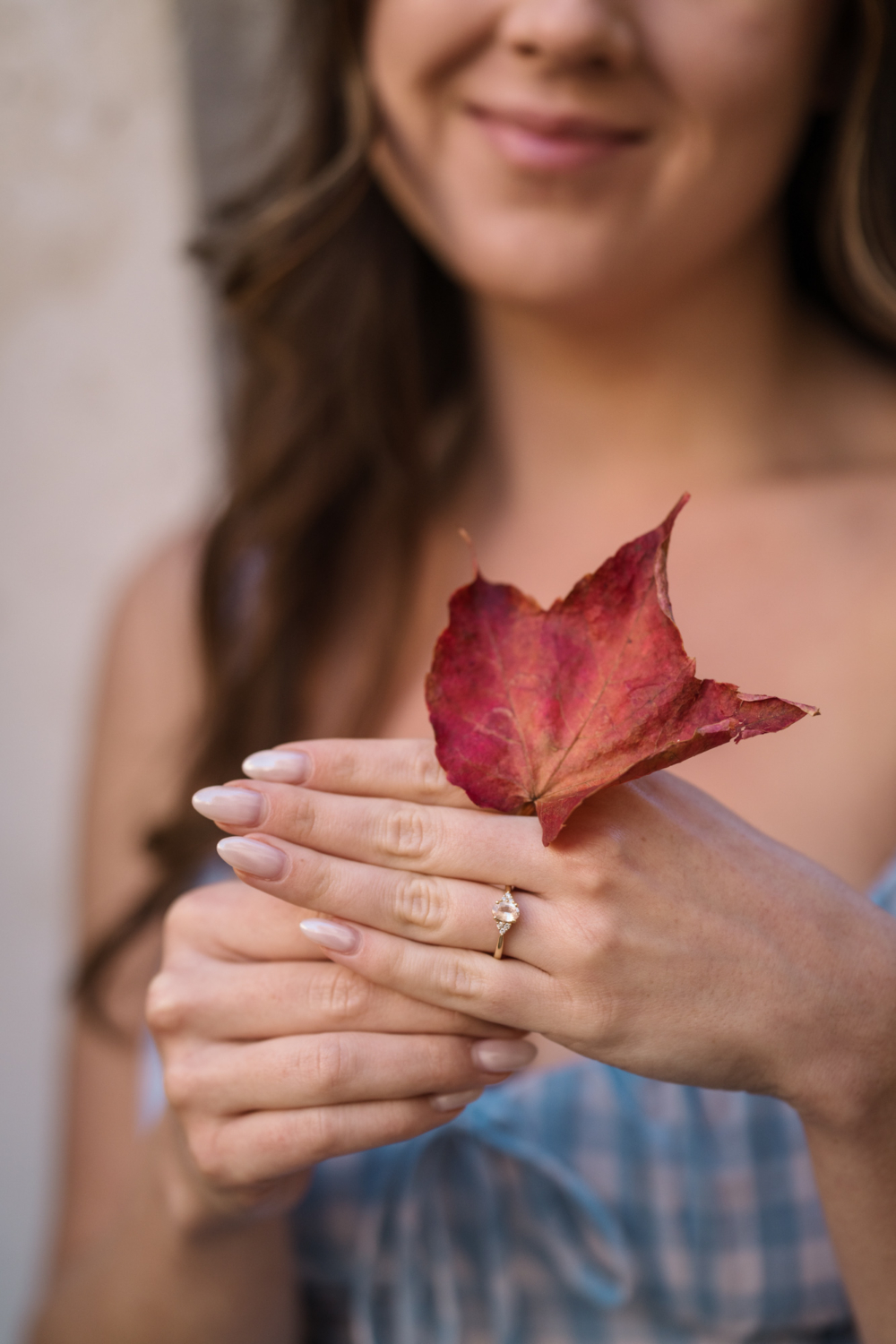 engaged woman holds autumn leaf with engagement ring