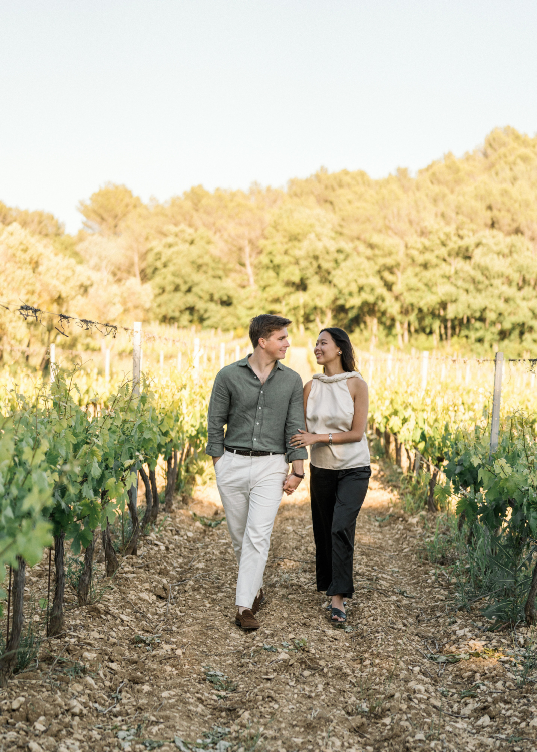 newly engaged couple walk hand in hand in vineyard