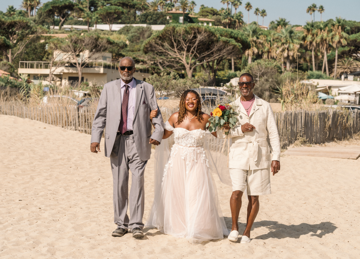 bride walks to her beach ceremony in saint tropez with dad and stepdad